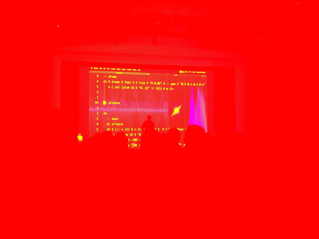 a livecoder on stage with tidalcycles code projected behind
