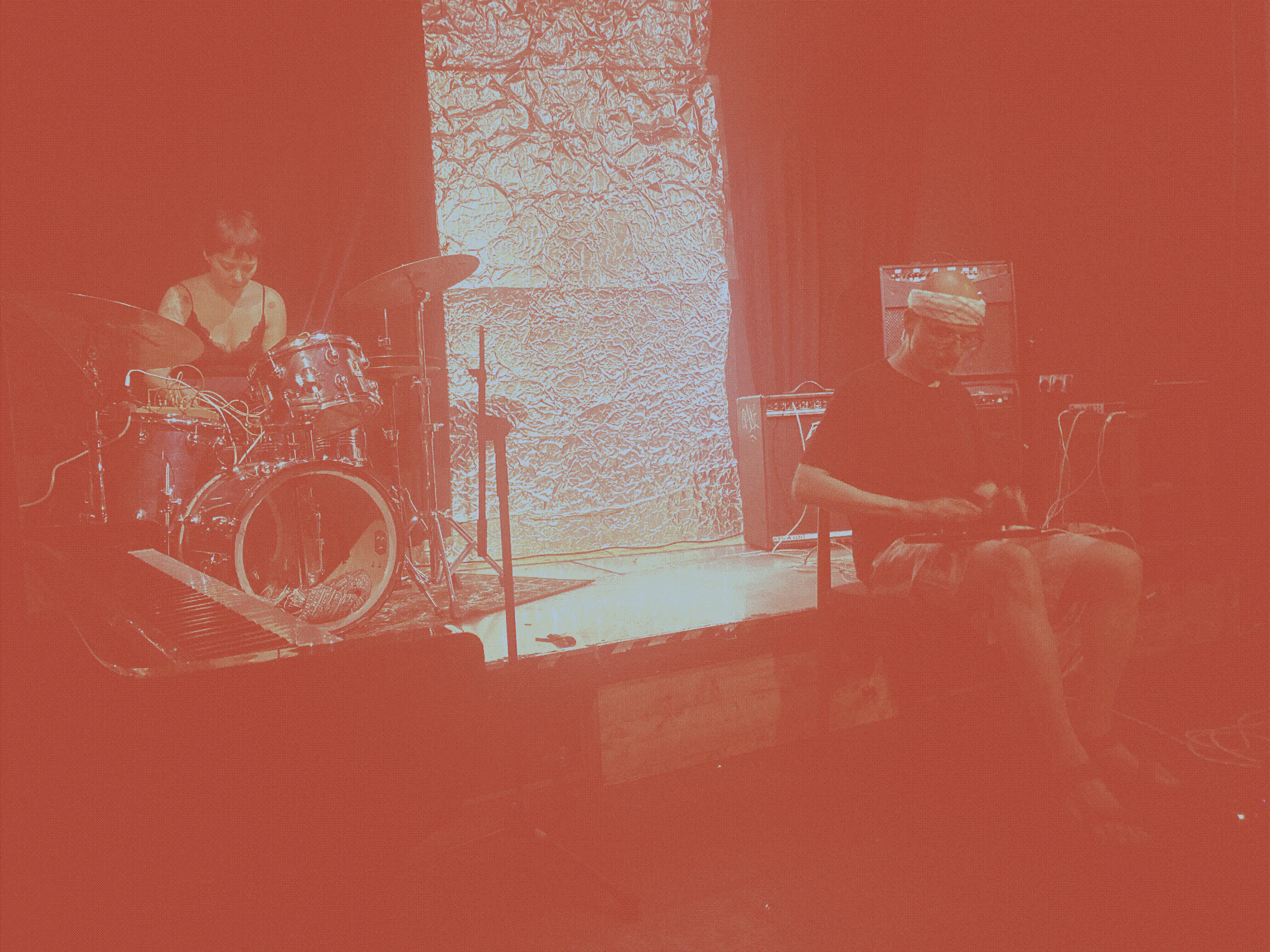 One of the assembled improv groups playing a weird guitar-like object with built-in effects and a performer twiddling strange synths laid on a drum set