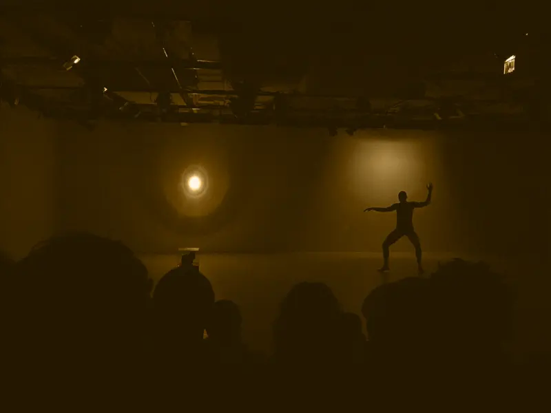 a performer stands with arms extended, 2 spotlights