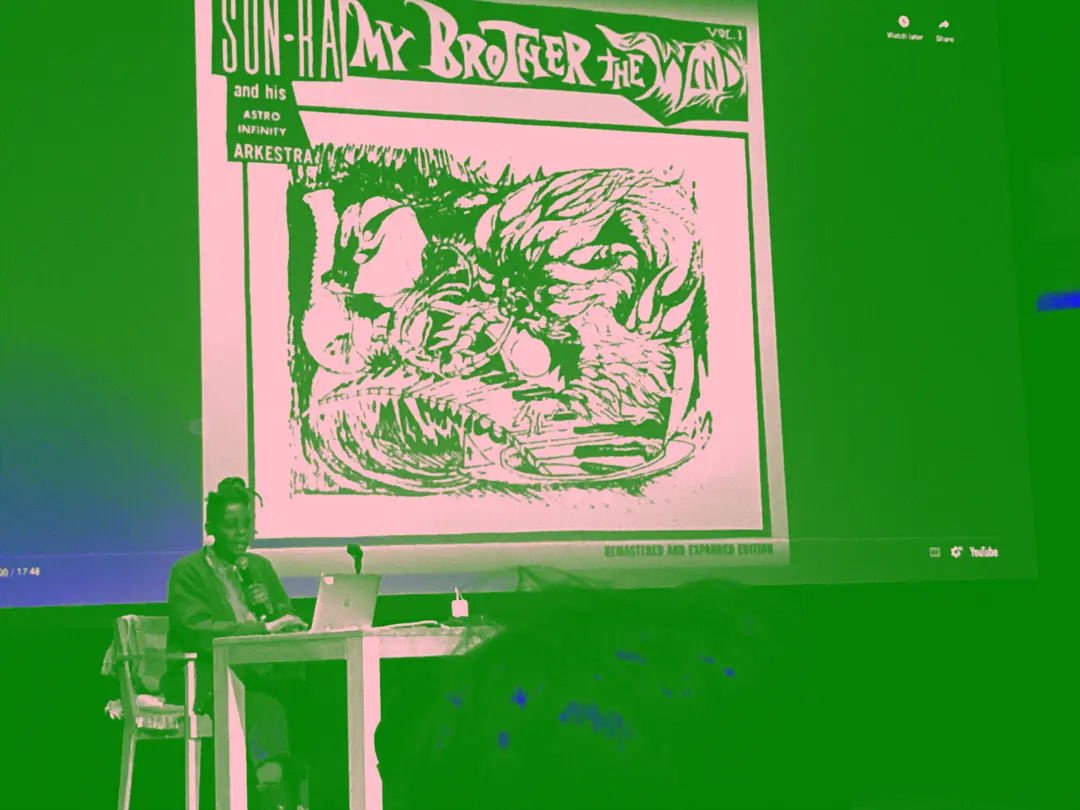 Lynnee Denise speaks in front of a slide of a Sun Ra album